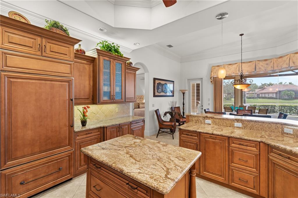 7833 Classics Drive Naples, FL 34113 - Photo 14 of 43 Kitchen with a kitchen island, decorative backsplash, hanging light fixtures, light tile patterned flooring, and light stone counters