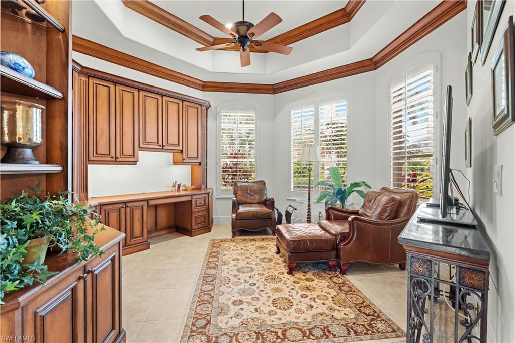 7833 Classics Drive Naples, FL 34113 - Photo 18 of 43 Living area featuring ceiling fan, a tray ceiling, light tile patterned flooring, ornamental molding, and built in desk