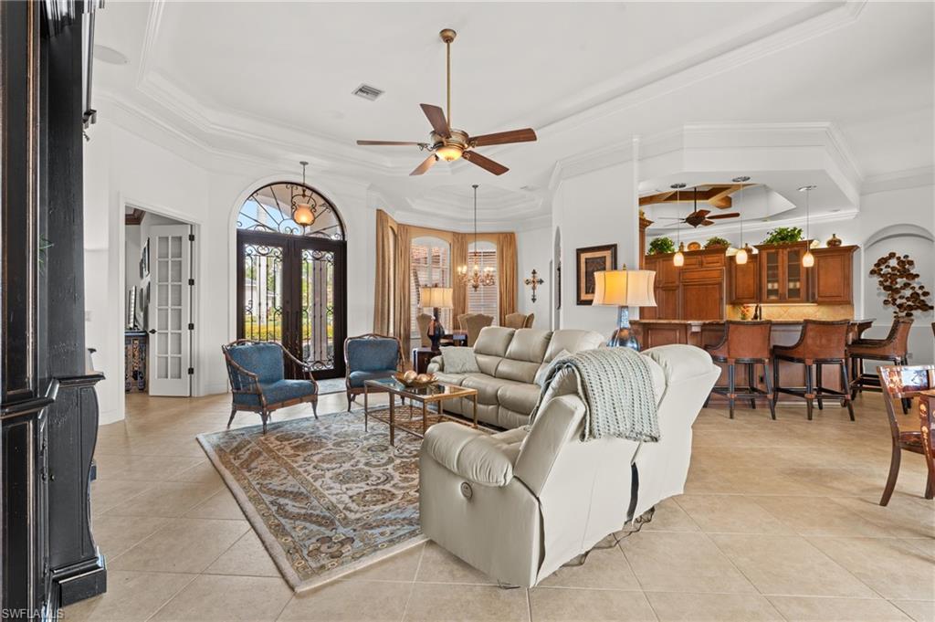 7833 Classics Drive Naples, FL 34113 - Photo 8 of 43 Tiled living room featuring ceiling fan with notable chandelier, a tray ceiling, ornamental molding, and french doors