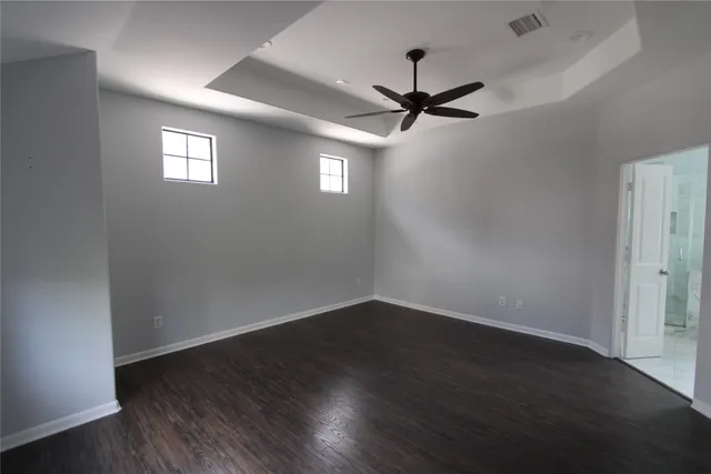 an empty room with wooden floor fan and windows