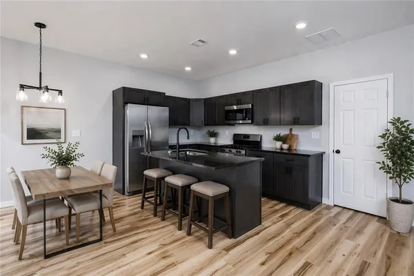 a kitchen with kitchen island granite countertop stainless steel appliances a refrigerator a stove a sink a dining table and chairs with wooden floor