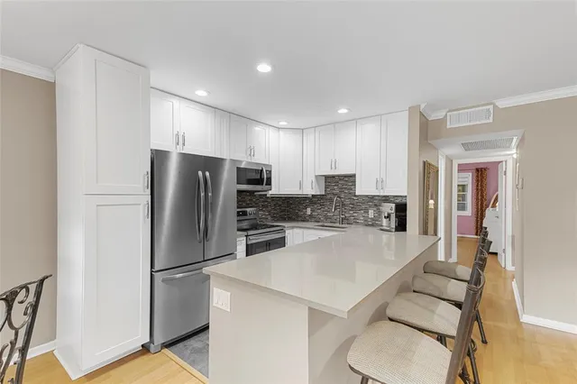 a kitchen with kitchen island a refrigerator a stove a sink and white cabinets with wooden floor