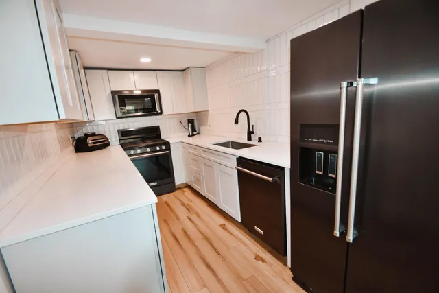 a kitchen with stainless steel appliances granite countertop a refrigerator a stove and a sink with wooden floor