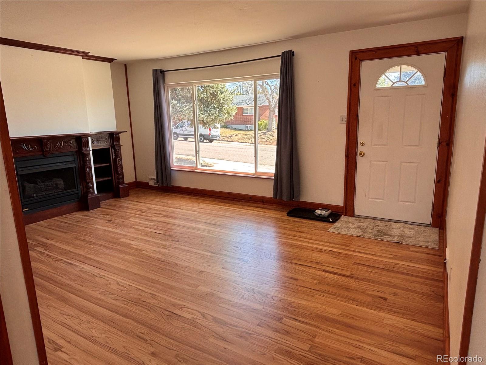2771 South Perry Street Denver, CO 80236 - Photo 7 of 40 an empty room with wooden floor fireplace and windows