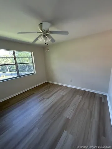 an empty room with wooden floor chandelier fan and windows