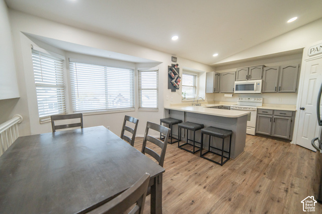 7676 Jefferson Road Magna, UT 84044 - Photo 5 of 24 Kitchen featuring wood-finish flooring, recessed lighting, gray cabinetry, white appliances, and a breakfast bar with seating