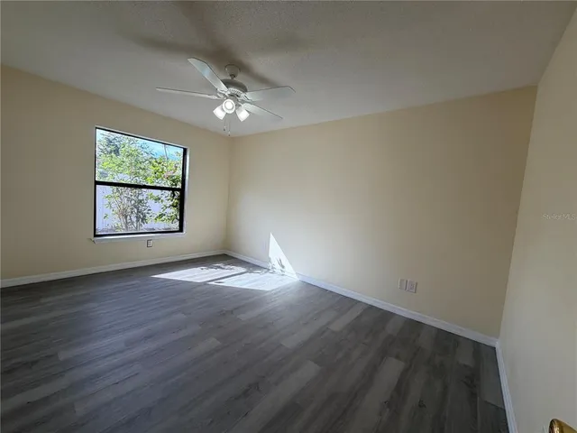 an empty room with wooden floor chandelier fan and windows