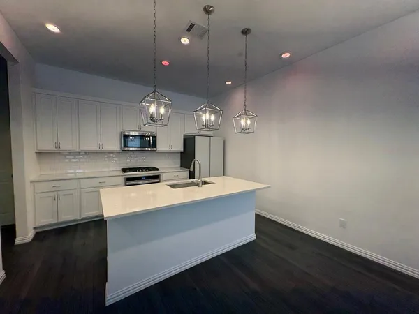 a large kitchen with granite countertop a stove a sink a refrigerator and a microwave oven on the wooden floor