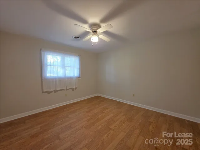 an empty room with wooden floor fan and windows
