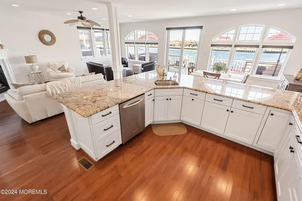 a spacious kitchen with stainless steel appliances granite countertop a sink dishwasher and white cabinets with wooden floor