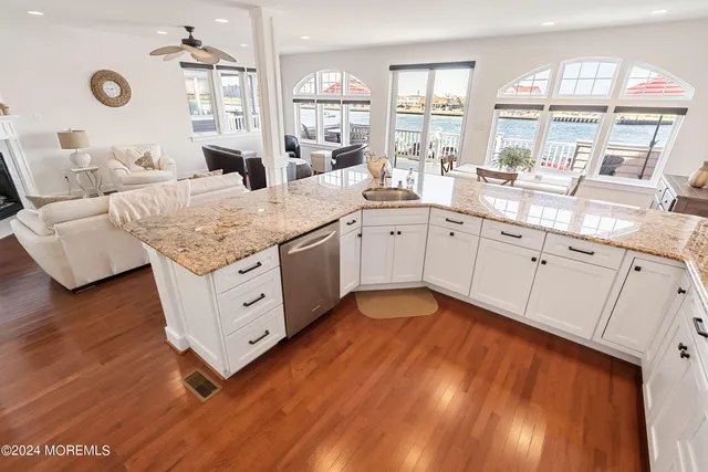 a spacious kitchen with stainless steel appliances granite countertop a sink dishwasher and white cabinets with wooden floor