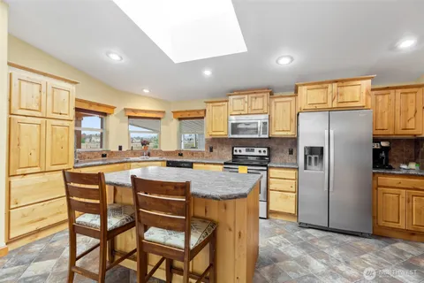 a kitchen with stainless steel appliances granite countertop a refrigerator a stove a sink a dining table and chairs with wooden floor