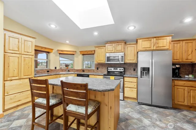 a kitchen with stainless steel appliances granite countertop a refrigerator a stove a sink a dining table and chairs with wooden floor