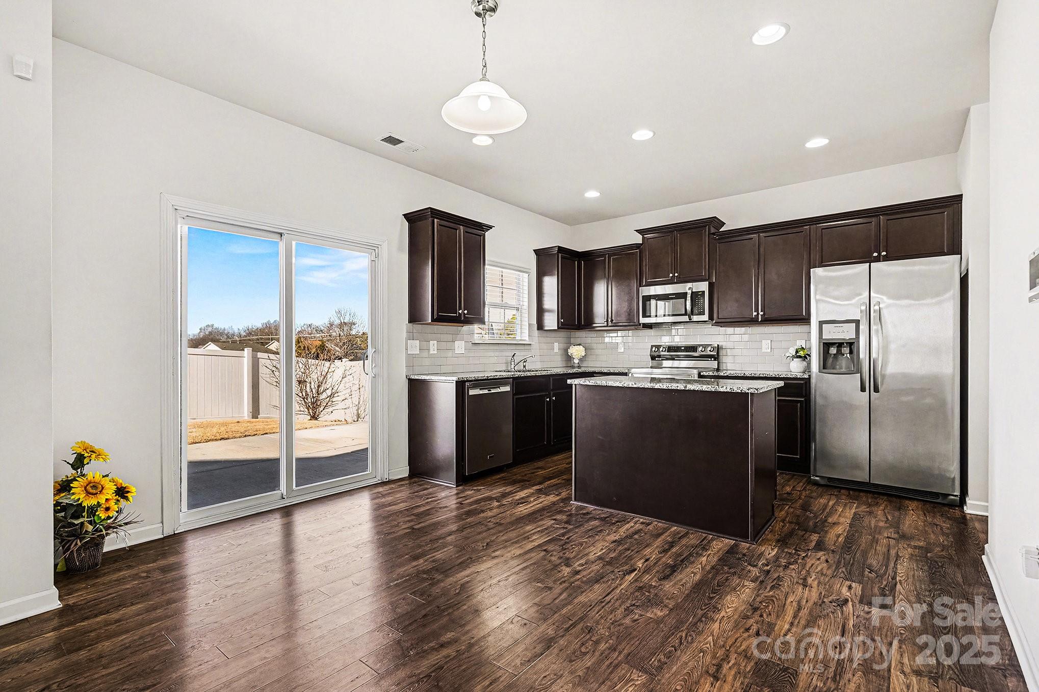 3224 Hawksbill Street Southwest Concord, NC 28027 - Photo 11 of 35 a kitchen with stainless steel appliances granite countertop a refrigerator oven a sink dishwasher a dining table and chairs with wooden floor