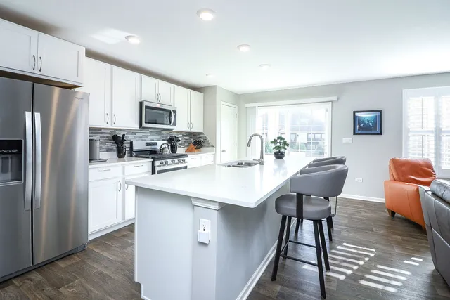 a kitchen with stainless steel appliances a dining table chairs refrigerator sink and cabinets