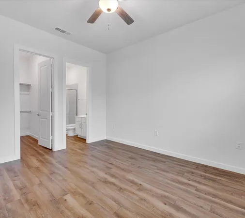 a view of an empty room with wooden floor and a ceiling fan
