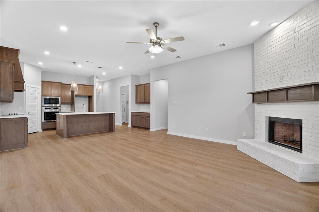 321 Skeen Peak Springtown, TX 76082 - Photo 13 of 37 Open-concept interior featuring light wood-finish flooring, a white brick fireplace with a wood mantel, a kitchen island with a white countertop, recessed lighting, and a ceiling fan