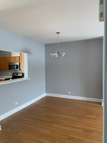 a view of empty room with wooden floor and kitchen