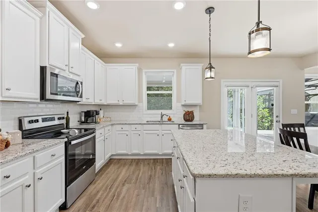 a kitchen with stainless steel appliances granite countertop a sink stove and white cabinets with wooden floor