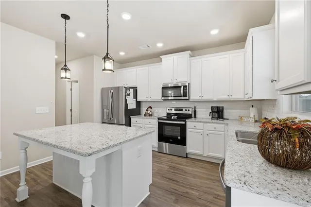 a kitchen with stainless steel appliances kitchen island granite countertop a stove a sink a refrigerator and white cabinets with wooden floor