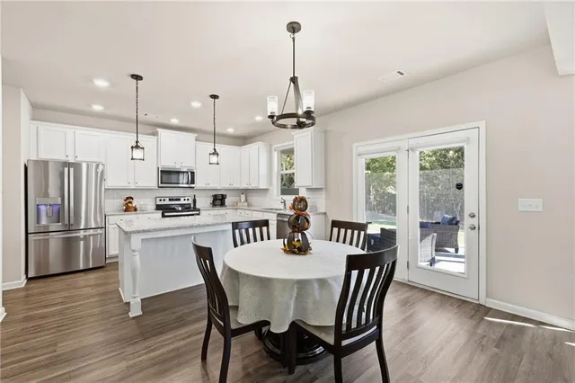 a view of kitchen with refrigerator a stove and a dining table with wooden floor