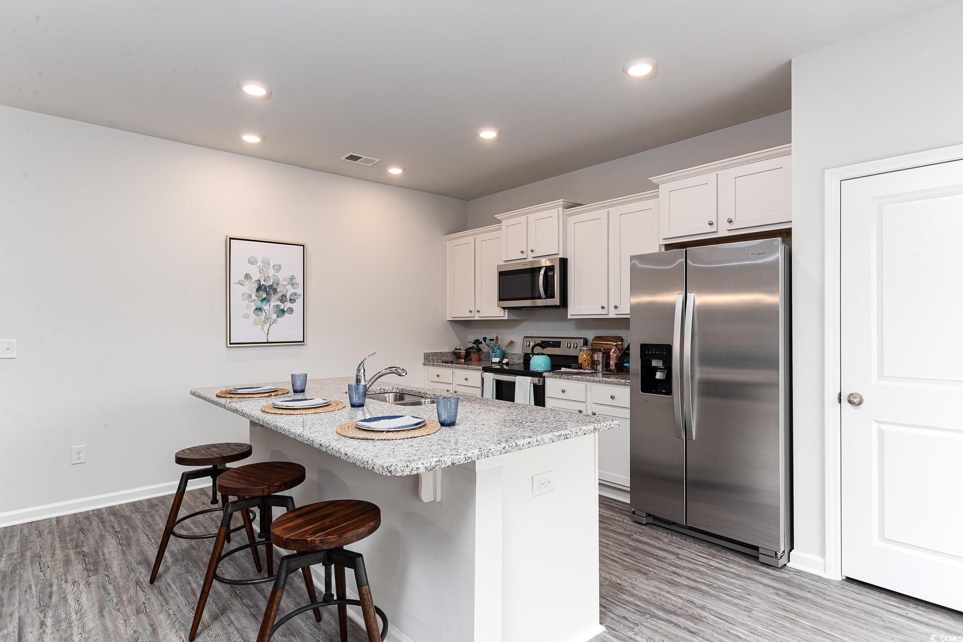1029 St Martin Street Georgetown, SC 29440 - Photo 3 of 23 Kitchen with appliances with stainless steel finishes, a kitchen bar, white cabinets, light wood-type flooring, and a kitchen island with sink