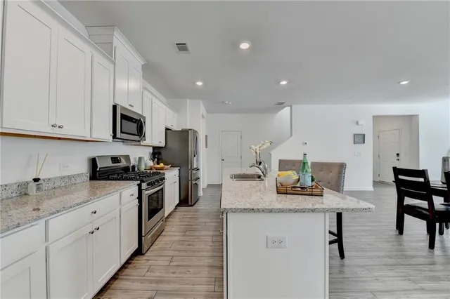 a kitchen with stainless steel appliances granite countertop a stove top oven a sink dishwasher a dining table and chairs with wooden floor