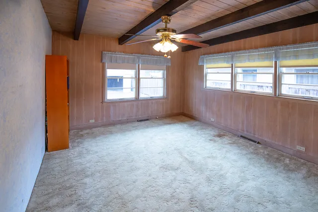 an empty room with chandelier fan and windows