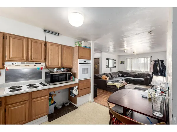 a living room with furniture a kitchen with stainless steel appliances kitchen island granite countertop a refrigerator a stove a sink dishwasher and white cabinets with wooden floor