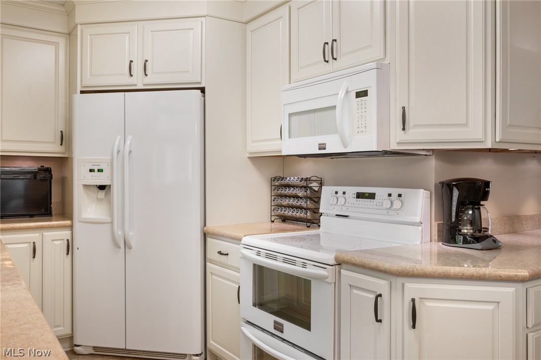 685 Sunnyside Road Vermilion, OH 44089 - Photo 18 of 50 Kitchen featuring white cabinetry with dark hardware, light-toned countertops, a side-by-side refrigerator, and a built-in microwave