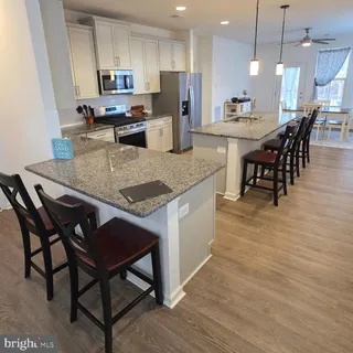 a kitchen with stainless steel appliances granite countertop a stove a refrigerator a kitchen island a dining table and chairs