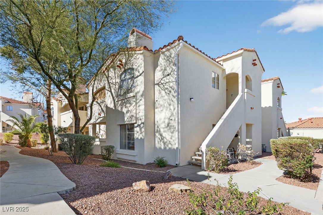 View of side of home featuring a tile roof, stucco siding, stairway, and a chimney
