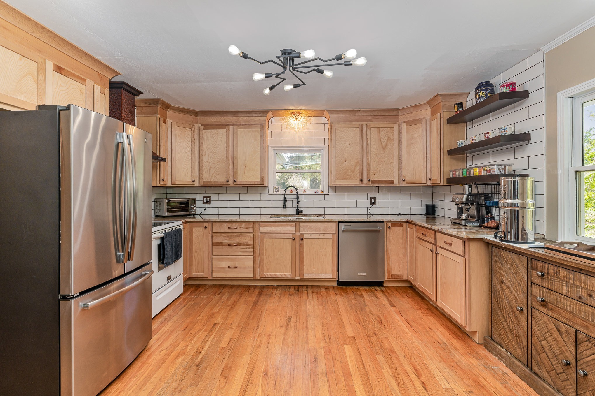 a kitchen with granite countertop a refrigerator a sink dishwasher a stove and white cabinets with wooden floor