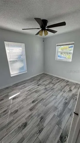 an empty room with wooden floor ceiling fan and windows