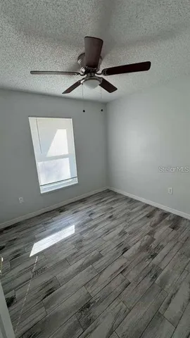 an empty room with wooden floor fan and windows