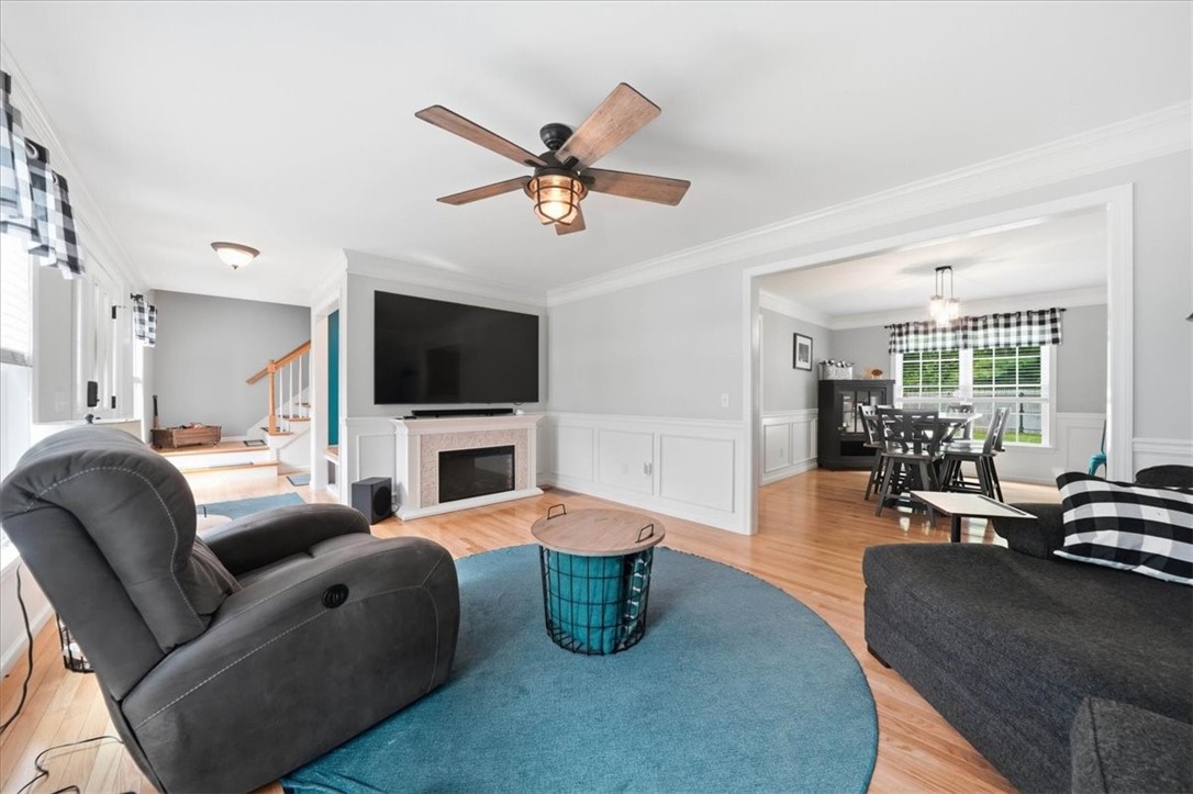 26 Davis Circle Warwick, RI 02886 - Photo 7 of 50 The inviting living room is warm, bright, and beautifully finished with gleaming hardwood floors, elegant crown molding, classic wainscoting, oversized windows, and a striking electric fireplace with custom surround.