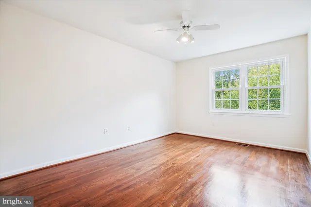 an empty room with wooden floor ceiling fan and windows
