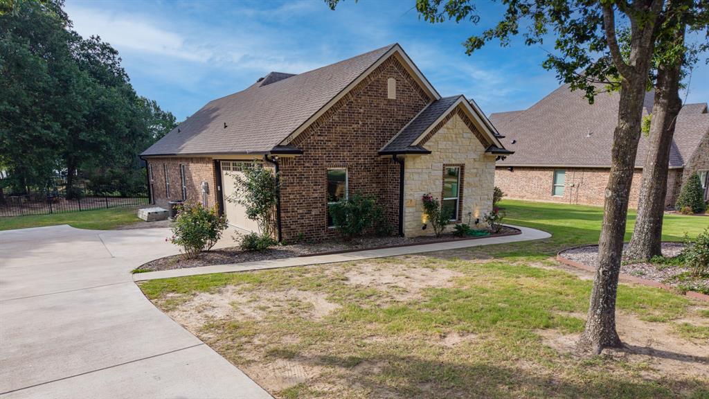 101 Lighthouse Lane Mabank, TX 75143 - Photo 31 of 40 Brick and stone exterior featuring a gabled roofline, concrete driveway, manicured landscaping, and mature trees