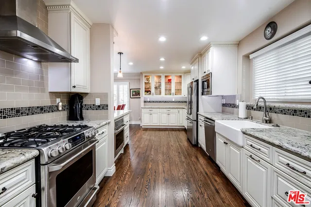 a kitchen with stainless steel appliances granite countertop a stove top oven a sink dishwasher and a refrigerator with wooden floor