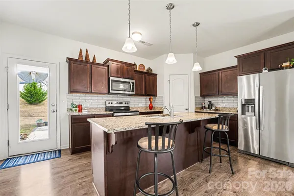 a kitchen with stainless steel appliances granite countertop a stove a refrigerator a kitchen island a sink dishwasher a dining table and chairs with wooden floor