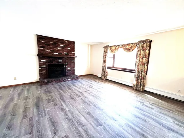 an empty room with wooden floor fireplace and windows