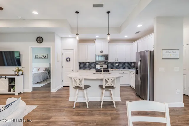 a kitchen with stainless steel appliances kitchen island granite countertop a refrigerator a stove a sink a dining table and chairs with wooden floor