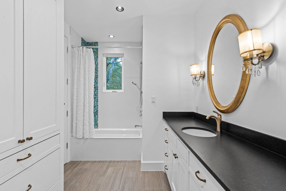 1905 Paisano Road Austin, TX 78746 - Photo 26 of 40 White cabinetry, a gold-framed mirror, and wood-look tile flooring elevate this functional and beautiful bathroom.