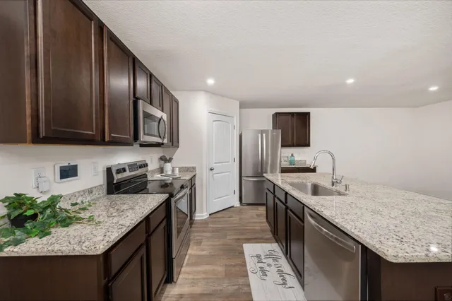 a kitchen with granite countertop stainless steel appliances a sink stove top oven and refrigerator