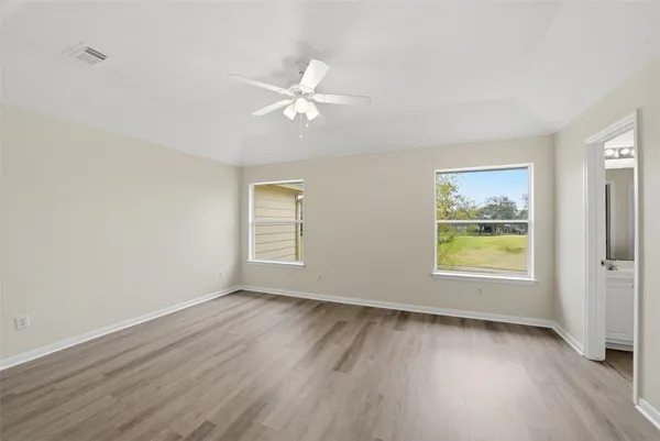 an empty room with wooden floor ceiling fan and windows
