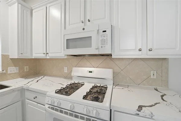a kitchen with white cabinets a sink stove and white countertops