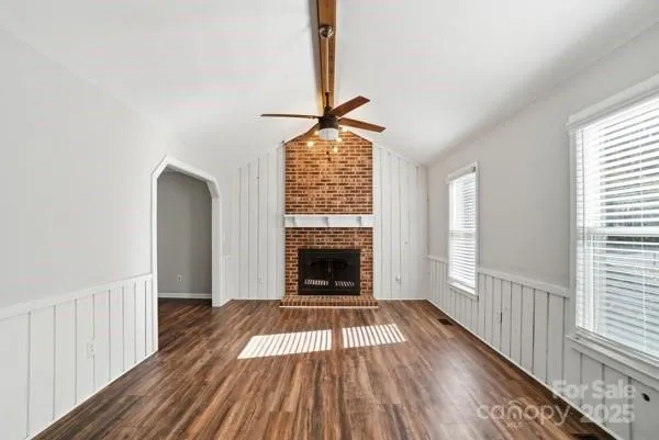 a view of an empty room with wooden floor fireplace and a window