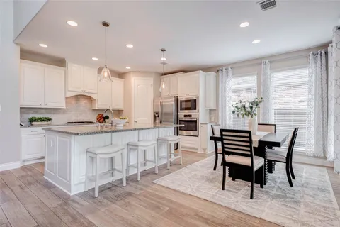 a kitchen with stainless steel appliances kitchen island granite countertop a stove a sink a refrigerator and white cabinets with wooden floor