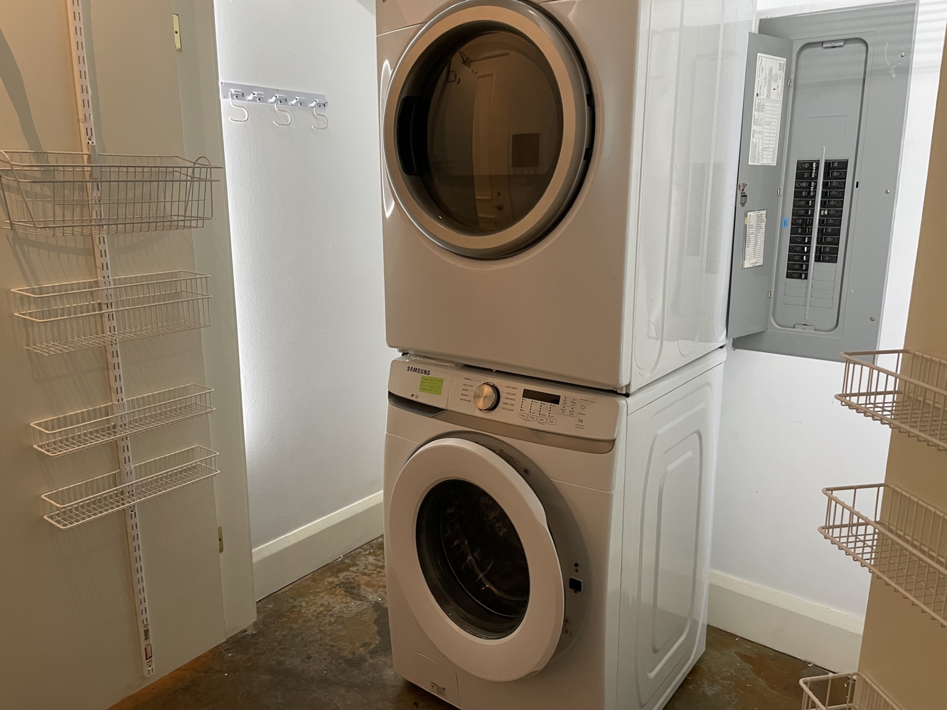 1401 Calumet Street, Unit 300 Houston, TX 77004 - Photo 26 of 31 This photo shows a compact laundry area with a stacked washer and dryer. It features wall-mounted storage racks and is adjacent to an electrical panel, suggesting efficient use of space.
