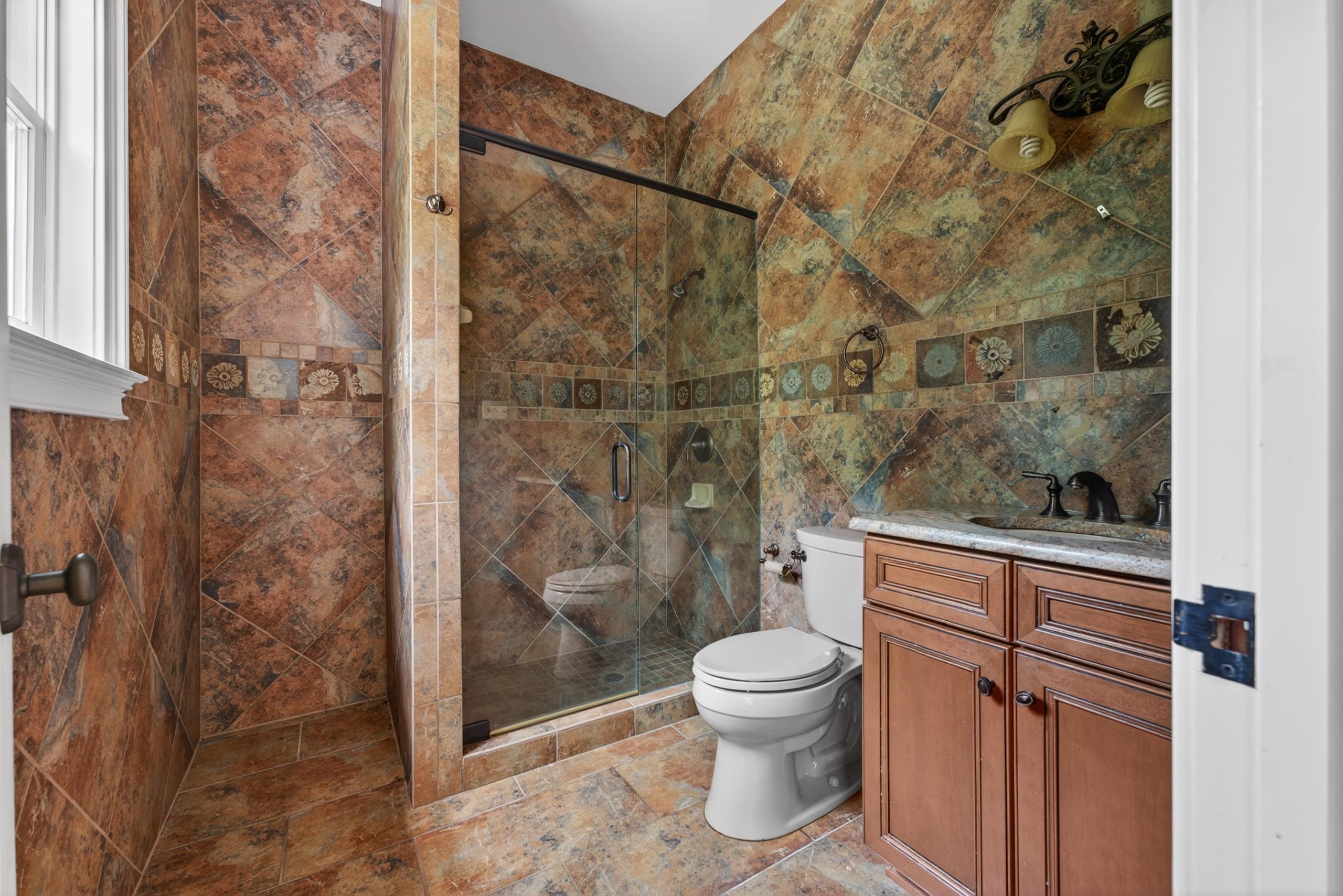 530 West Raines Road Memphis, TN 38109 - Photo 32 of 38 Bathroom featuring a glass-enclosed shower, rich-toned tile flooring and walls, a built-in wood-finish vanity with a stone countertop, and a window for natural light
